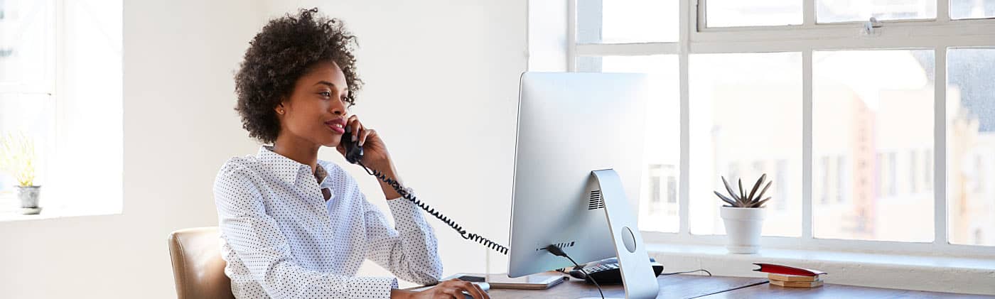 Woman in an office looking at laptop while on the phone discussing open enrollment 