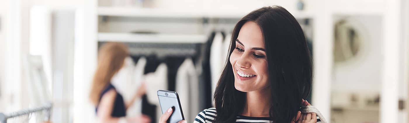 A woman tracks her latest purchase on her smartphone in a boutique: money-saving strategy