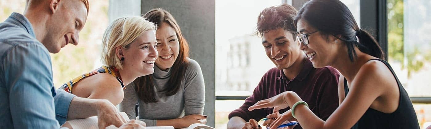 young adults smiling and studying together at a table adulting