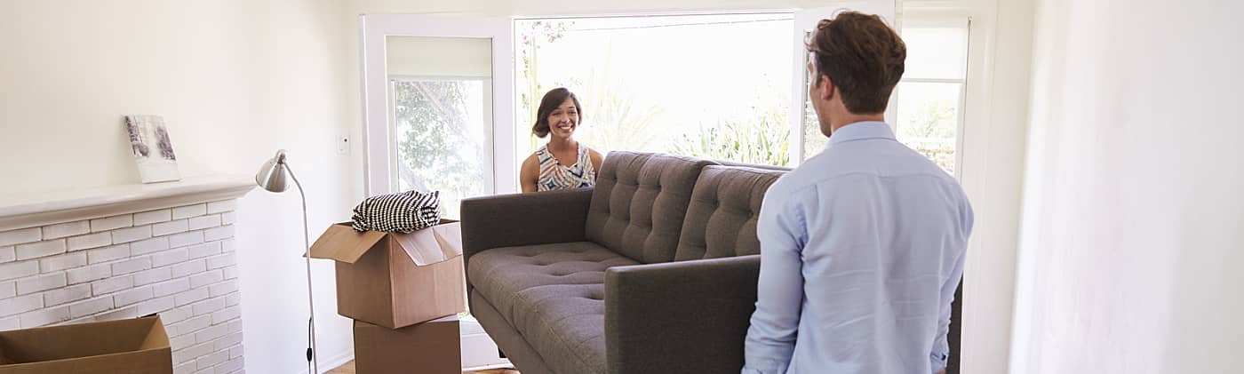 young couple carries a sofa into the living room of their new house as they discuss managing debt