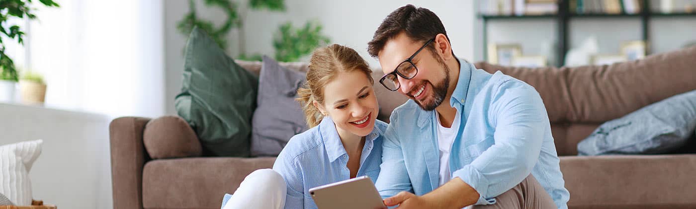Young couple sitting on the floor and looking up the 2019 ira contribution limits on tablet 