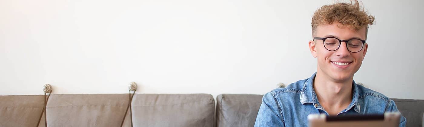 male college student sits on a couch at home and uses tablet computer for managing student loan debt