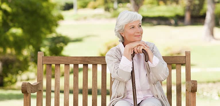A old woman sitting on a park bench smiling after retiring single