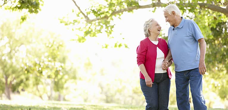 A retired couple smiles as they walk together in a park on a spring day: variable annuity 