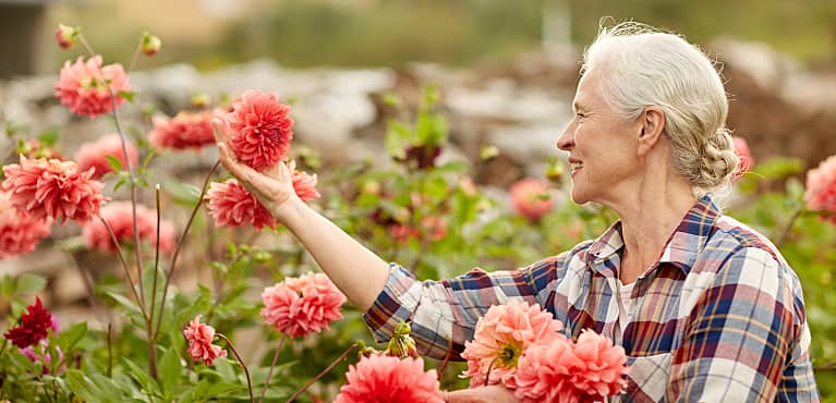 retired woman holds flower bloom in her garden and thinks about options for cash value life insurance