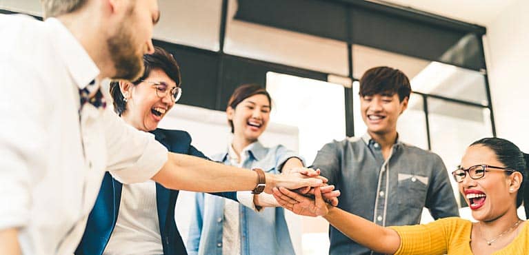 group of young professionals pile up hands in a huddle and wonder if they need to buy life insurance