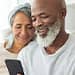 Happy mature couple on a couch looking up average retirement savings by age on a phone