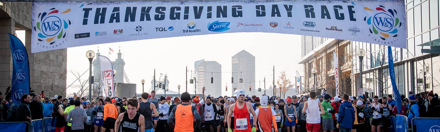 runners preparing for thanksgiving day race under starting line banner with participating company sponsors