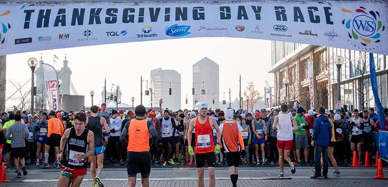 runners preparing for thanksgiving day race under starting line banner with participating company sponsors